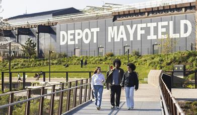 People walking in park with Depot Mayfield behind them